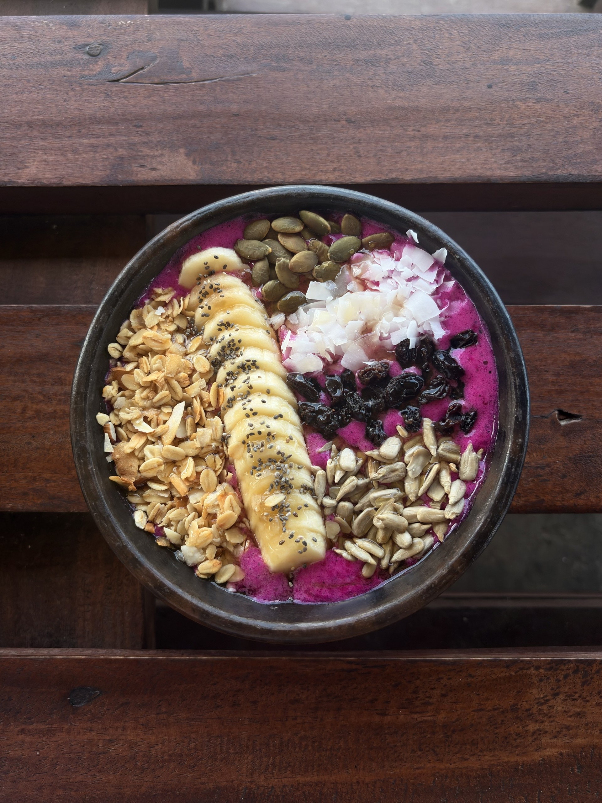 Frühstücksbowl mit Drachenfrucht, Banane und Granola auf einem Holztisch