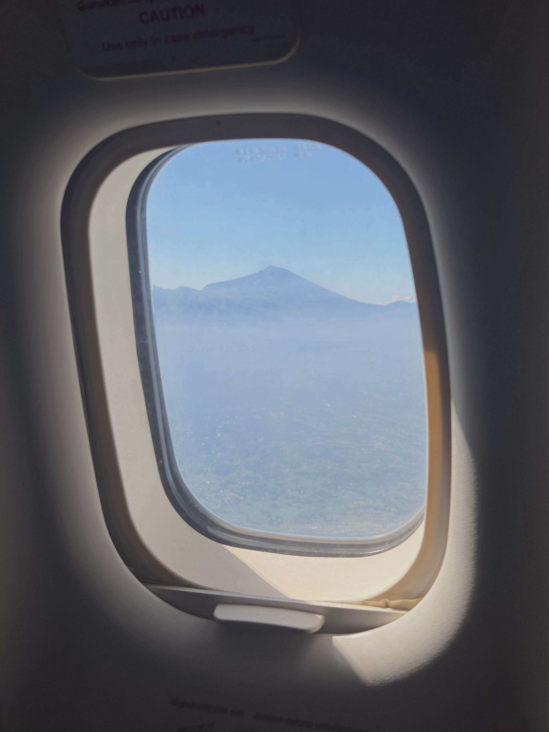 Blick aus dem Flugzeugfenster auf einen Vulkankegel über dem Dunst