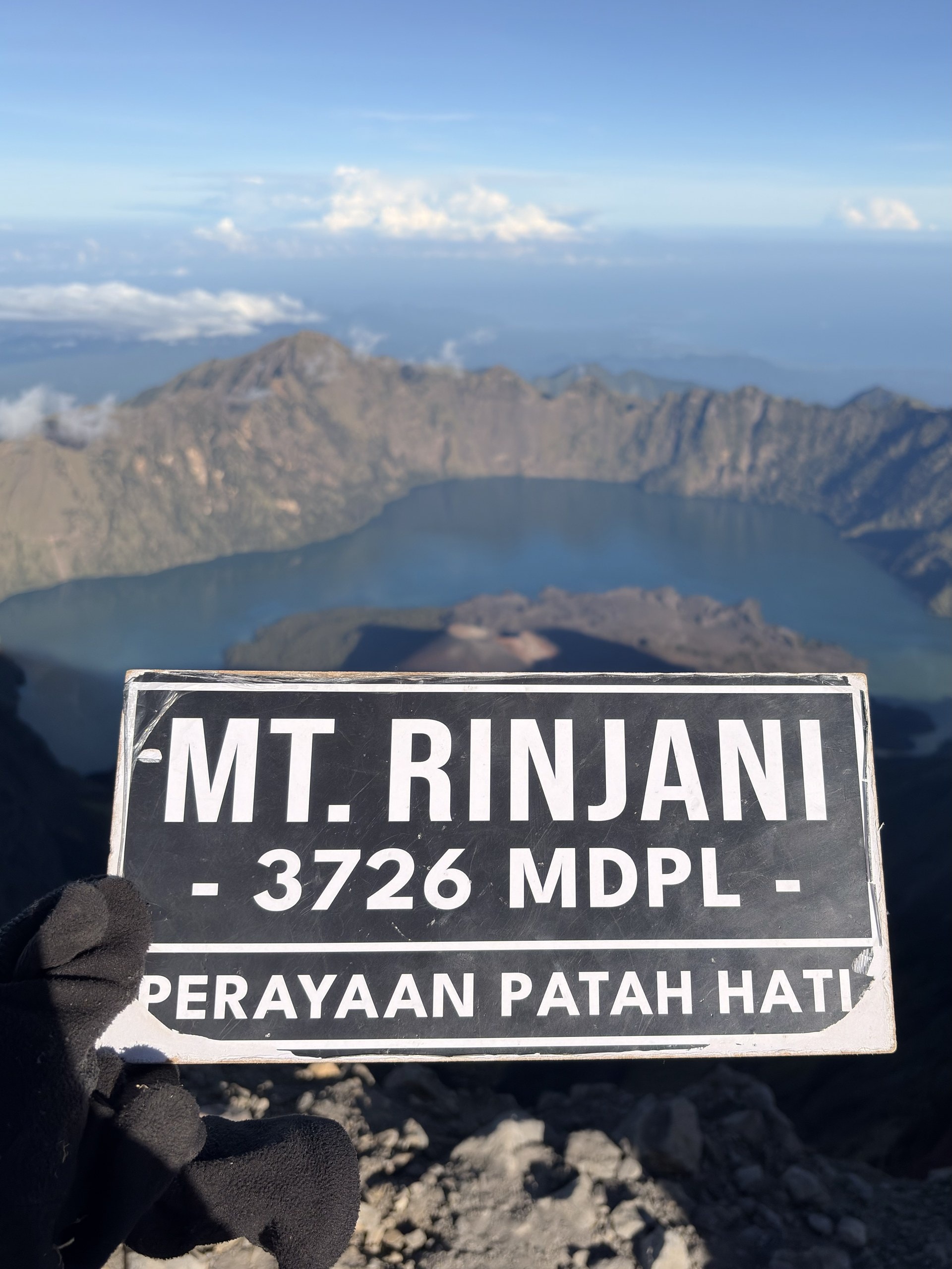 Das Gipfelschild des Mount Rinjani auf 3.726 Metern, dahinter der Krater