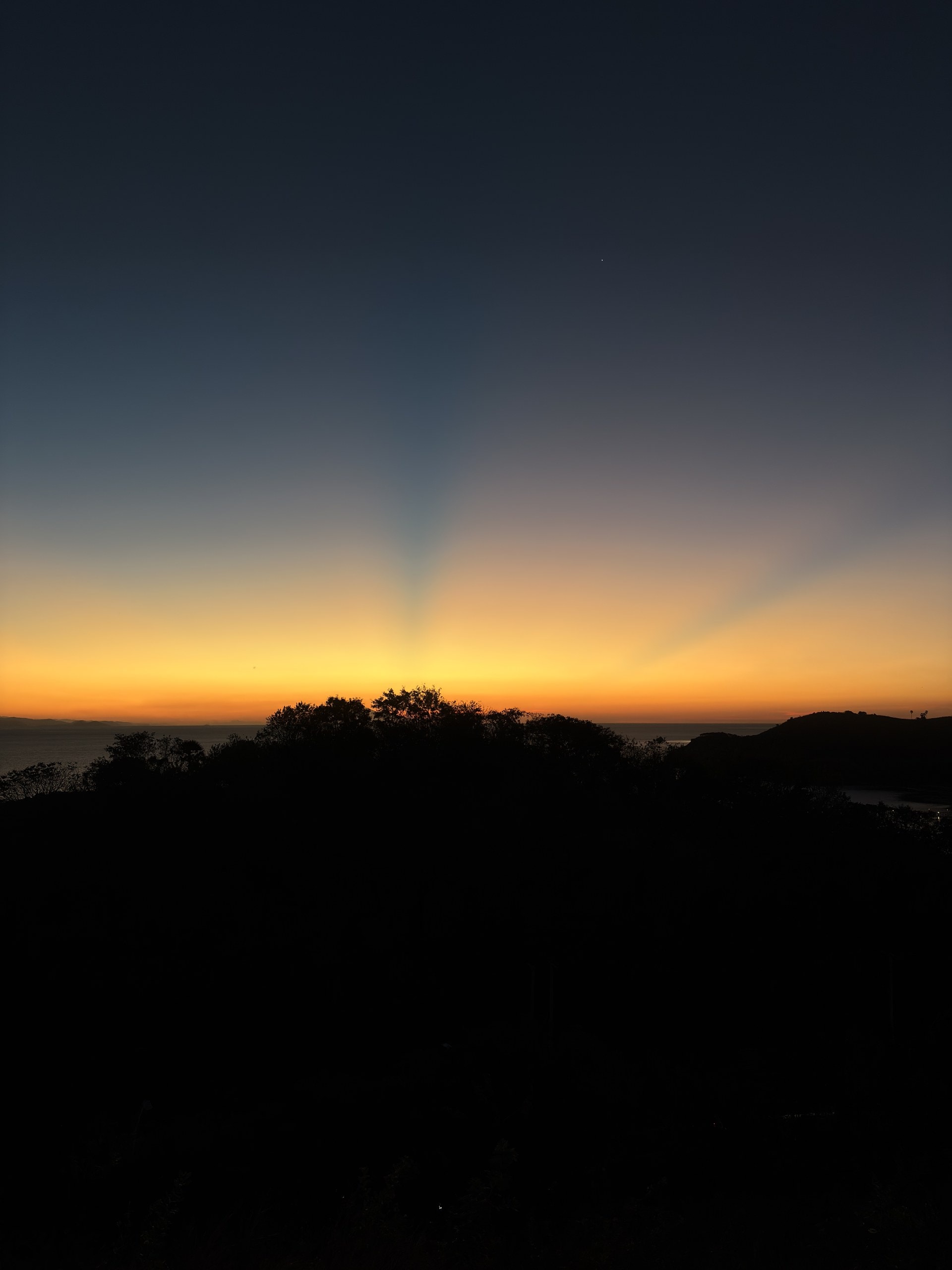 Sonnenuntergang hinter einem bewaldeten Bergrücken am Meer
